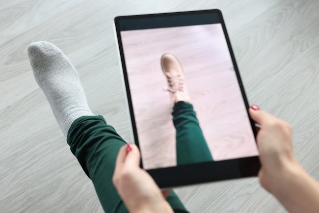 A close-up of a smartphone screen displaying an augmented reality application. The app shows a pair of virtual shoes superimposed on the user's feet, standing on a living room rug. The lighting is natural, and the focus is sharp on the virtual shoes and the user's feet.